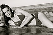 Portrait of attractive blonde woman wearing bikini lying on side on beach, black and white