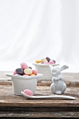 White egg cup filled with colourful sugar eggs and Easter bunny figurine on wooden surface