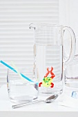 Toy frog in carafe with water with straw in glass of water