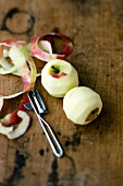 Peeled apples with peeler on wooden surface