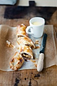 Apple strudel cut in pieces with knife and vanilla sauce in cup on baking paper