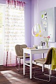 Small dining area below pendant lamp and curtain with pattern of birds in room with lilac walls