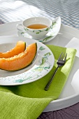 Plate of sliced fruit on tablecloth with bowl of sauce on tray