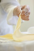 Close-up of hands holding rolled out pasta dough