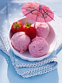 Three scoops of strawberry ice cream with fresh strawberries and a cocktail umbrella