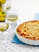 Zucchini and herb quiche in serving dish and two glasses of white wine