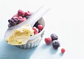 Vanilla ice-cream on spoon lying over a bowl of frozen berries