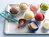 Various types of ice cream in tubs with an ice cream scoop
