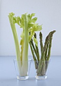 Asparagus and celery in glasses on white background