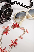 Close-up of sunglasses, red coral necklace and headphones on white background