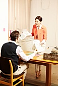 Bürosituation, Frau mit Unterlagen vor Mann am Schreibtisch am Schalter