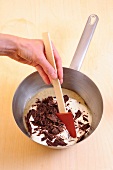 Close-up of hand stirring chocolate with cream in sauce pan to prepare dessert, step 3