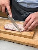 Hand carving skin of duck breast in rhombic shapes on wooden board
