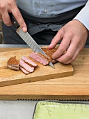 Hand cutting duck breast into slices on wooden board