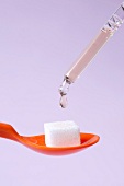 Close-up of autogenous vaccine drop falling from pipette on sugar cube in spoon