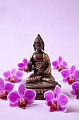 Statue of Buddha with orchid flowers on pink background