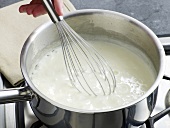 Mixing ingredients with whisk in saucepan for preparation of bechamel sauce , step 4