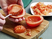 Tomato seeds being removed with spoon for preparation of tomato concasse , step 1