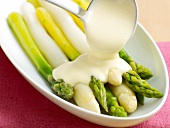 Close-up of hollandaise sauce being poured on asparagus in serving dish 