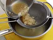 Mixture being strained through sieve for preparation of white butter sauce, step 1