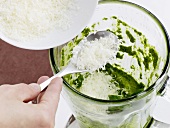 Close-up of grated pecorino cheese being added to pesto in grinder, step 2