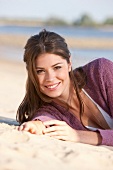 Portrait of pretty brunette woman lying on the beach, smiling