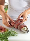 Close-up of hand wrapping salmon trout with fillets on white background