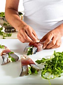 Close-up of hand wrapping fish and herbs with ham
