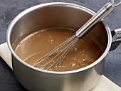 Close-up of bright coloured sauce being whisked in pot