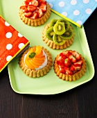 Different fruit tartlets with tissue paper on green serving tray