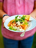 Woman holding goat cheese with melons on plate, garden kitchen