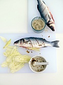 Two sea bass sprinkled with fennel and salt on chopping board