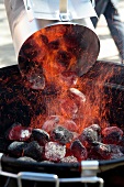 Brennende Holzkohle wird in einen Grill geschüttet