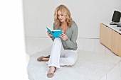 Blonde woman engrossed in reading John Wilde's book while relaxing in living room