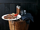 Plate of grilled steak with glass of water, napkin, salt and pepper mill on wooden block