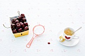 Cherries in cardboard box, sieve and espresso cup on white background