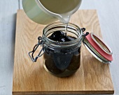 Syrup being poured on black nuts in jar