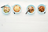 Four plates with different dishes of pasta on white background