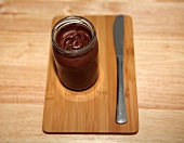 Chocolate cream in glass jar with knife on wooden platter