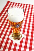 A glass of beer with a head of foam on a red and white checked tablecloth