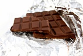 Schokolade liegt auf Silberpapier, ein abgebrochener Riegel daneben.
