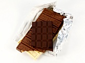Stack of chocolate bars on silver foil on white background