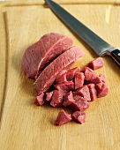Pieces of beef with knife on chopping board