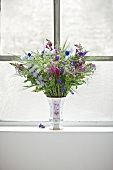 Vase with different types of flowers on window sill