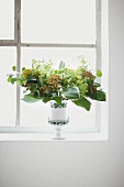 Vase with leaves and flora on window sill