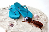 Pair of blue flip flips and sunglasses in sand with shells