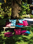 Colourful cushions on wooden bench and grass