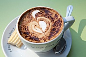 Close-up of coffee with heart shaped cream design in cup with spoon and cookie on plate