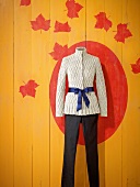 White braided peplum jacket with blue bow and black jeans against patterned wall