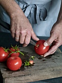 Close-up of stem of tomato being cut for preparation of tomato sauce, step 1